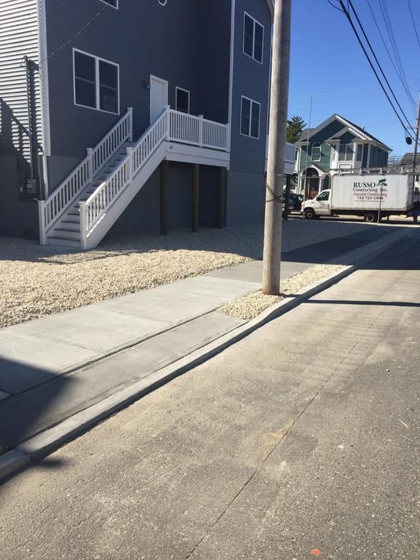 A gray building with white stairs, a sidewalk, a utility pole, and a truck on a sunny day.