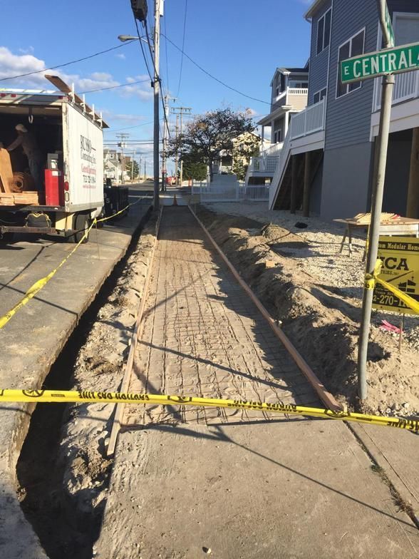 Construction site: Trench dug in street, yellow caution tape, utility truck, pipeline.