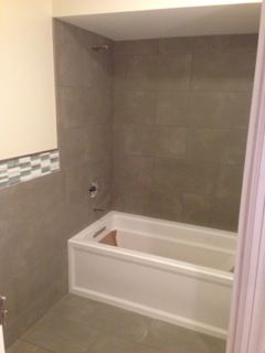 Bathroom with white tub, gray tile, and accent tile near the wall.