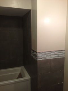 Bathroom corner with a dark gray tiled area, white bathtub, and mosaic tile border.