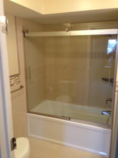 Bathroom with tub and sliding glass shower doors. White tub and walls, beige tiles, and a white toilet.
