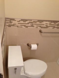 Toilet in a bathroom with beige tiles, mosaic border, and a chrome grab bar and toilet paper holder.