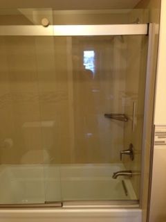 Clear glass shower door on a white tub, with silver fixtures and light-colored tile.