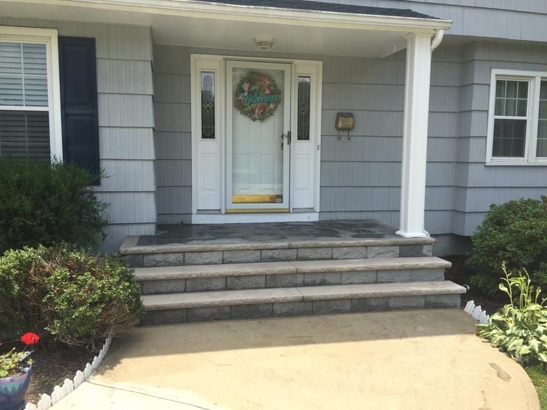 Grey brick steps lead up to a white door on a house with grey siding.
