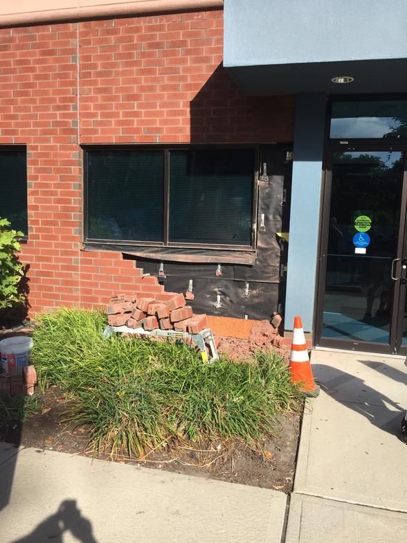 Damaged brick wall beside a window with exposed structural elements, and a pile of bricks on the ground.