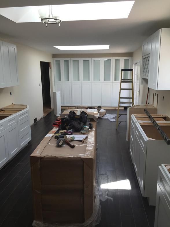Kitchen remodel in progress; white cabinets, dark wood floor, island with tools on it.
