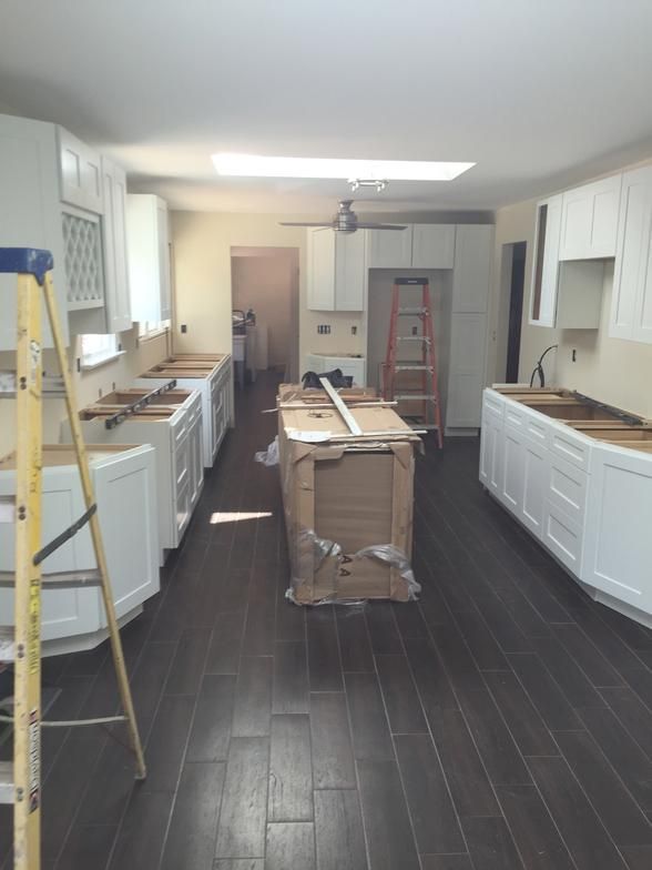 Kitchen remodel in progress with white cabinets, dark wood floors, and an island.