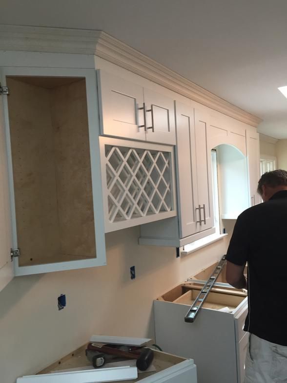 Kitchen cabinets being installed; a worker measures below a wine rack.