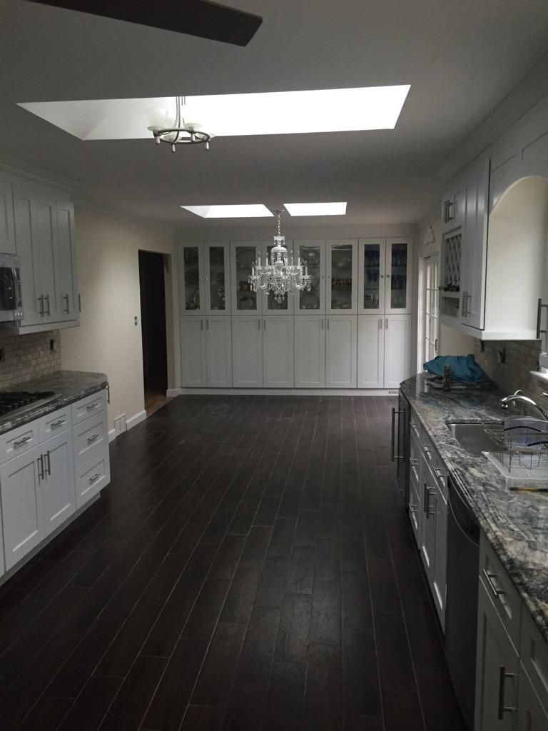 Spacious kitchen with dark wood floors, white cabinets, and a chandelier. Skylights brighten the room.