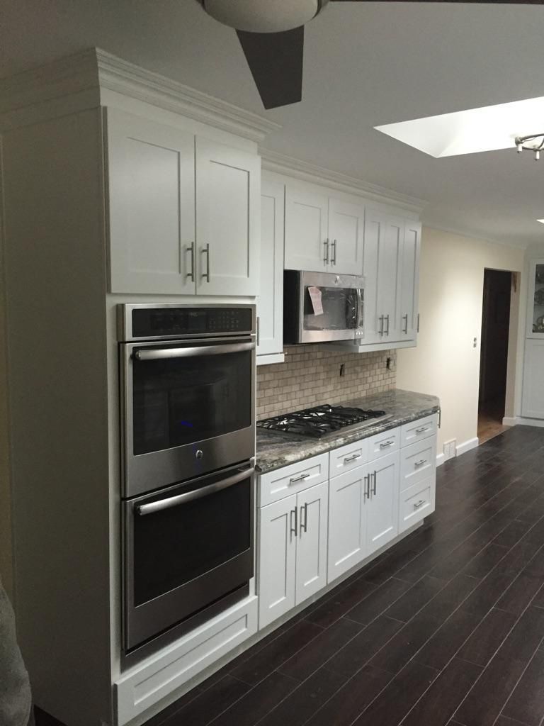 White kitchen cabinets with stainless steel appliances and dark wood flooring.