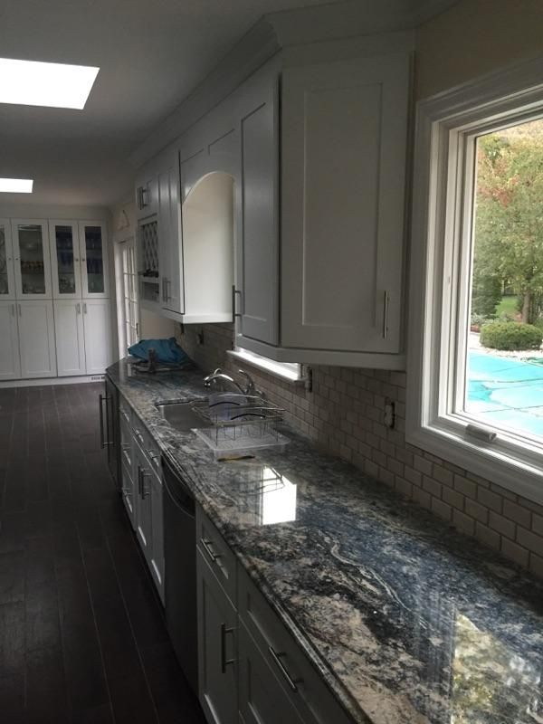 White kitchen cabinets with dark granite countertop, tile backsplash, and a window overlooking a pool.