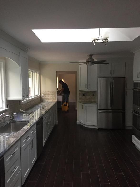 Spacious kitchen with white cabinets, dark wood floor, granite countertop, and a person in the background.