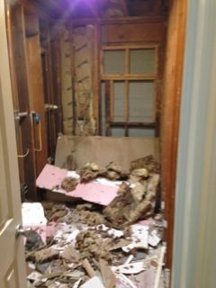 A demolished room interior, debris scattered, exposed walls, small window.