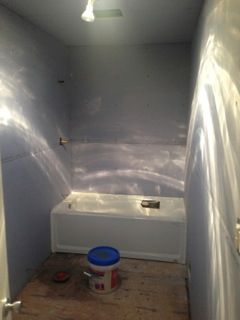 Small bathroom renovation in progress with bathtub, blue walls, and paint bucket on floor.