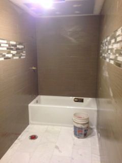 Bathroom under construction; white tub, brown wall tiles, accent mosaic tiles, bucket.