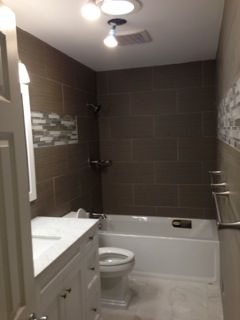 Bathroom with brown tiled shower, white tub, toilet, vanity, and neutral floor.