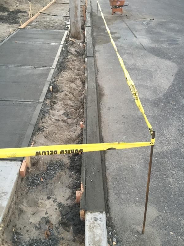 Construction site with newly poured concrete curb, trench, and yellow caution tape.