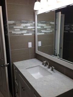 Bathroom with white vanity, mirror, and patterned tile accent.