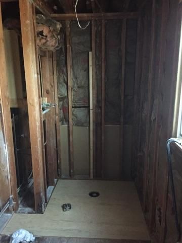 Bathroom renovation in progress. Wooden studs, plywood floor with drain, partial walls.