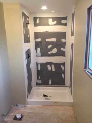Bathroom under construction; shower stall with gray cement board and white pan, unfinished.