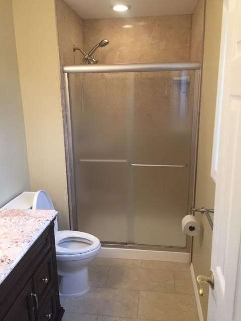 Bathroom with shower, toilet, and vanity. Beige walls and frosted glass shower doors.