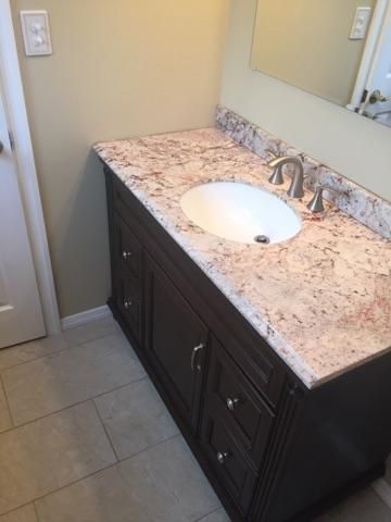 Dark brown vanity with a granite countertop, a white oval sink, and a chrome faucet in a bathroom.