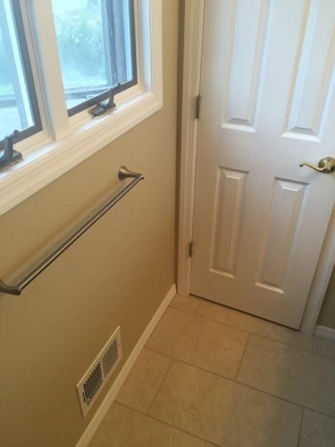 Beige bathroom corner with towel bar, window, closed white door, and tiled floor.