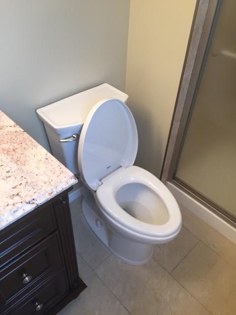 White toilet with the lid up in a bathroom next to a vanity with a granite countertop.