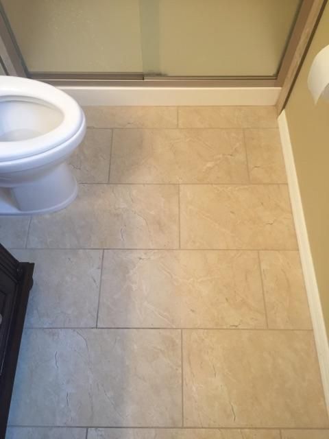 Beige tile floor in a bathroom with a white toilet on the left and a shower door and wall.
