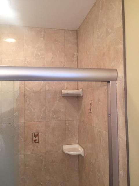 Shower stall with beige tile walls, glass door, and silver frame. Soap dishes and shower controls are visible.