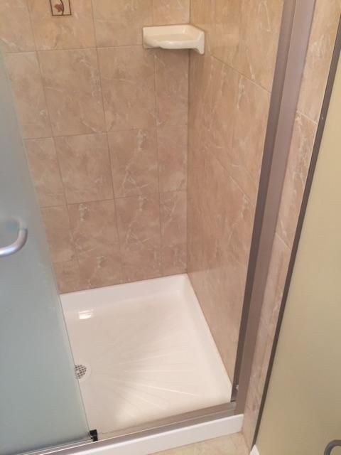Shower with beige tile walls, white shower base, and glass door. A soap dish is mounted on the wall.
