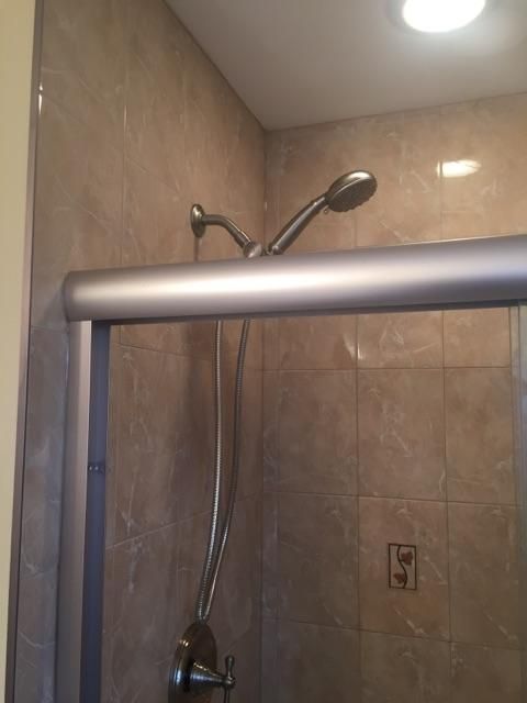 Shower interior with brown tiled walls, silver shower head and controls, and a glass sliding door.