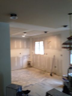 Interior of a kitchen under construction. Drywall walls, recessed lights, and exposed studs.