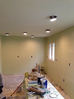 A room with light green walls, recessed lighting, and a countertop with paint supplies.