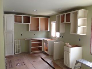 Kitchen with unfinished cream cabinets, empty spaces, and light green walls.
