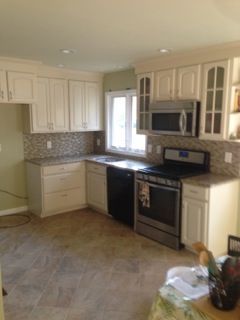 White kitchen with light countertops, tile backsplash, stainless steel appliances, and beige tile flooring.