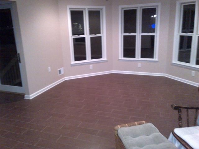 A sunroom with dark brown tiled floor, beige walls, and white-framed windows; a glass door is visible.