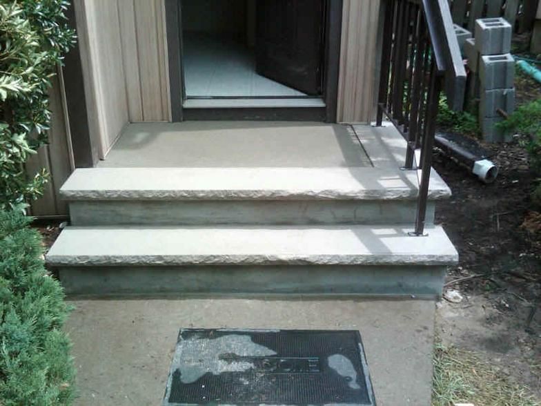 Concrete steps leading to a doorway with a black railing.