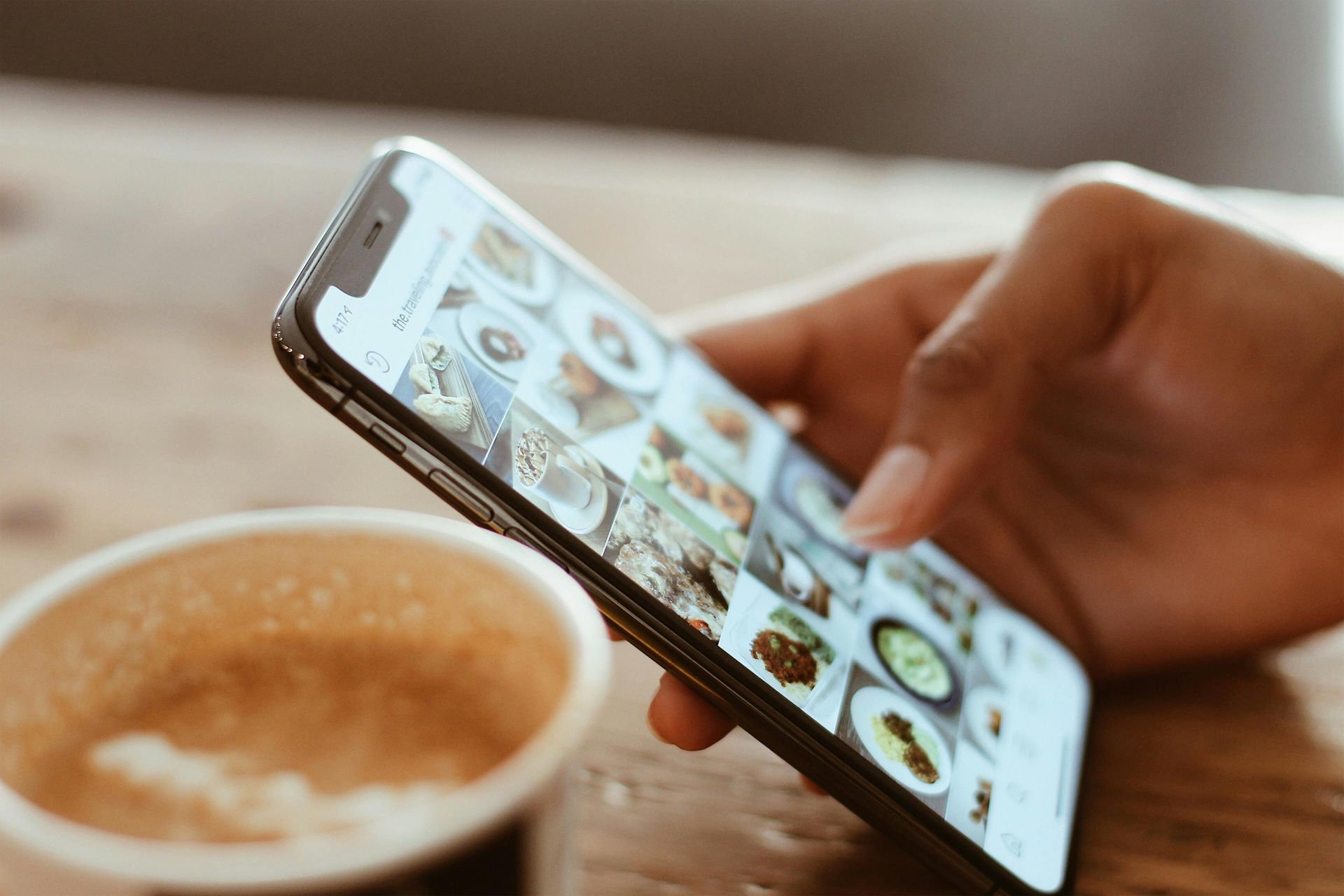 A person is holding a cell phone next to a cup of coffee.