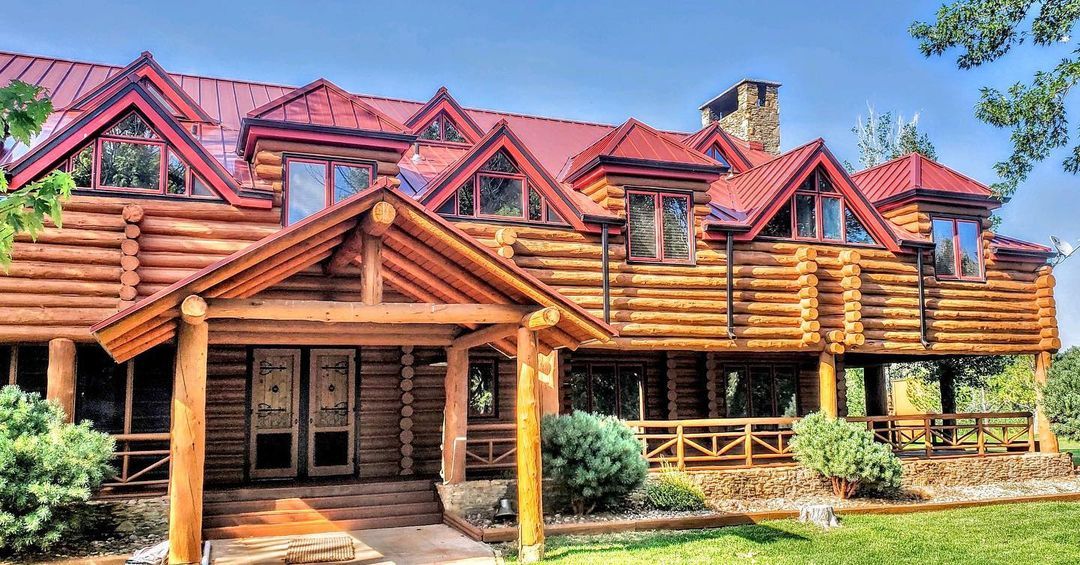 Log cabin home with a red roof and wooden beams on a sunny day.