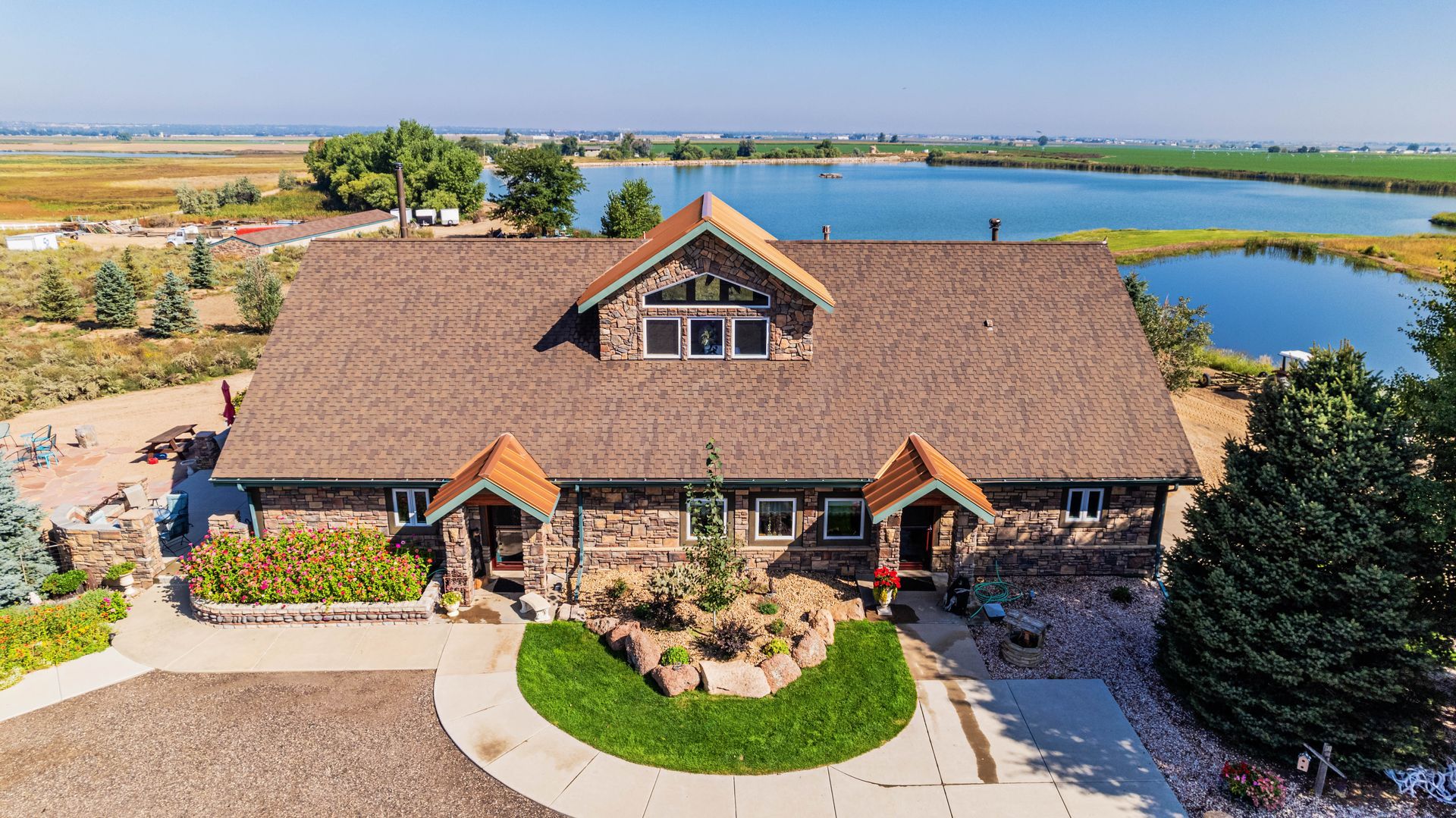 Stone house with brown roof by a lake on a sunny day.