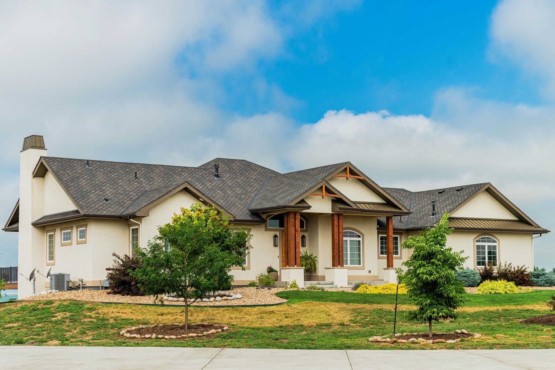 Beige stucco house with dark gray roof and a blue sky.