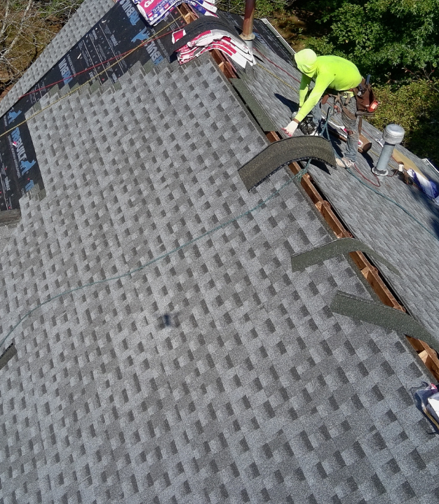 The roof of a house is getting a full roof replacement and the crew has began laying synthetic underlayment. Surrounding areas have been covered with a blue tarp for protection.