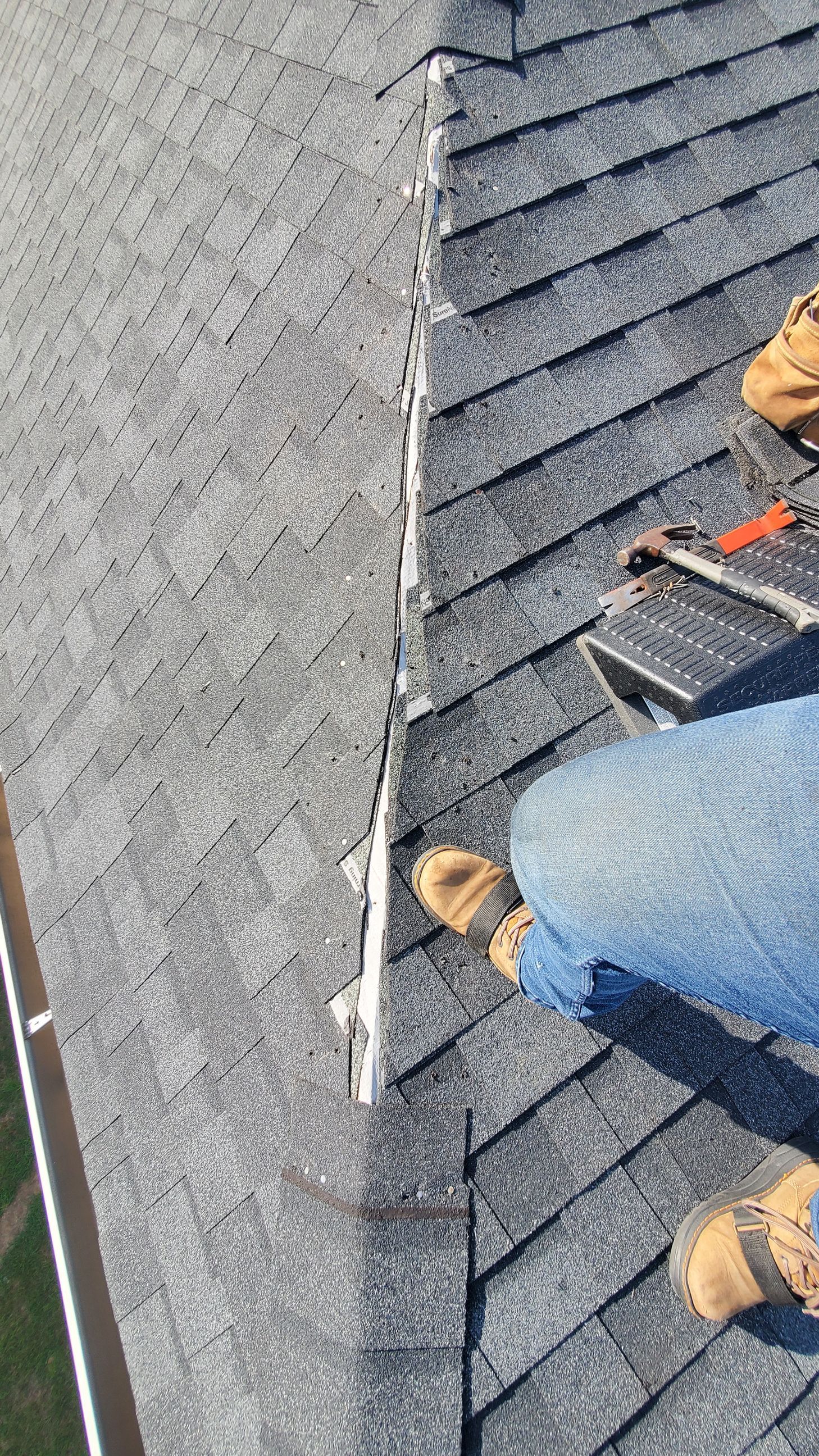 Roofer on a roof, removing shingles near a vent. Roof has missing and damaged shingles.
