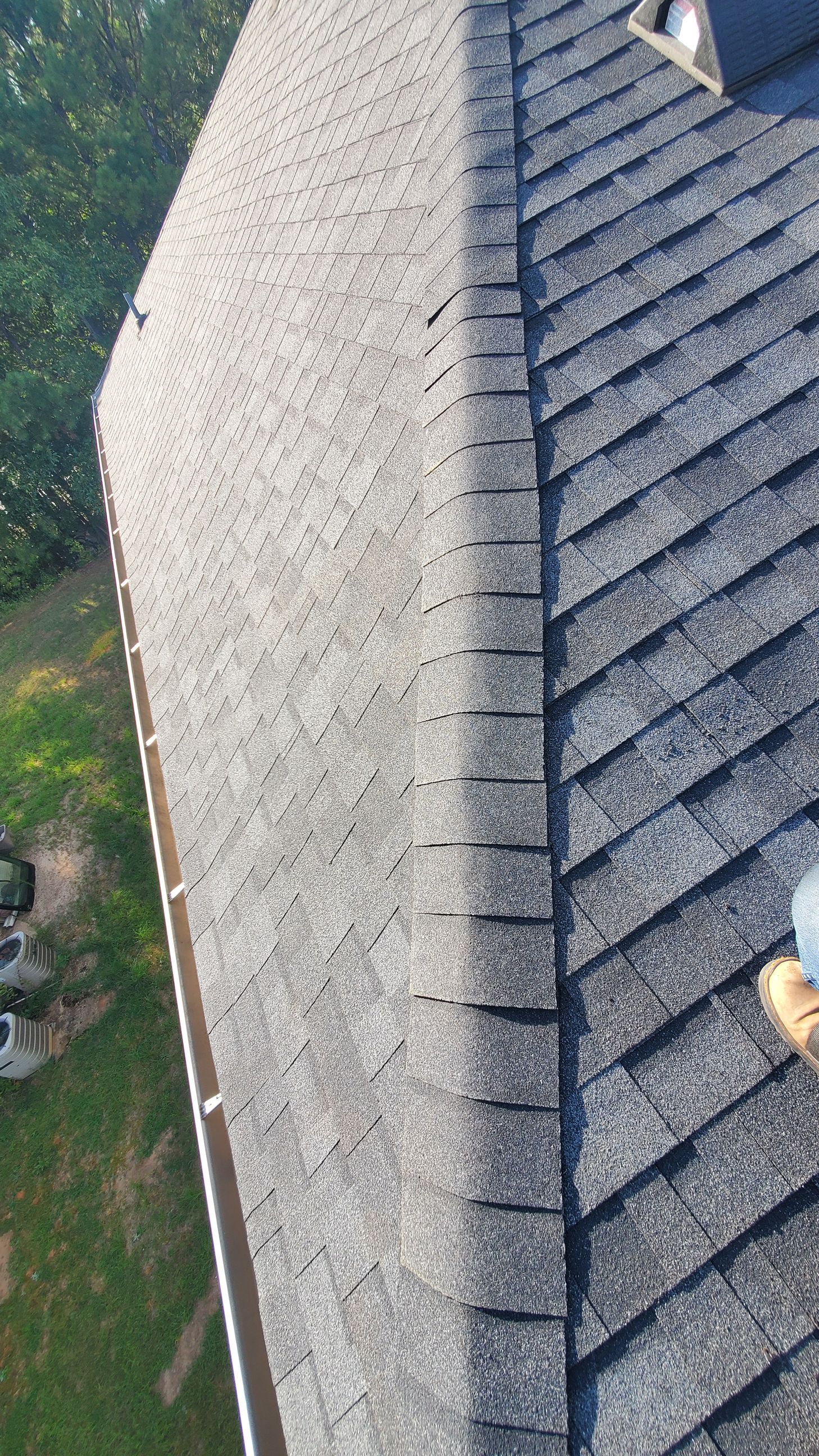 A person on a roof, blue jeans, brown boots, working near the gutter, asphalt shingles.