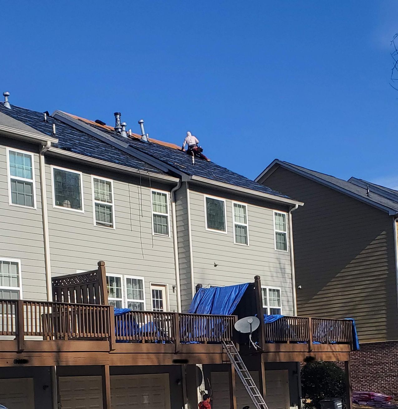 The roof of a house is getting a full roof replacement and the crew has began laying synthetic underlayment. Surrounding areas have been covered with a blue tarp for protection.