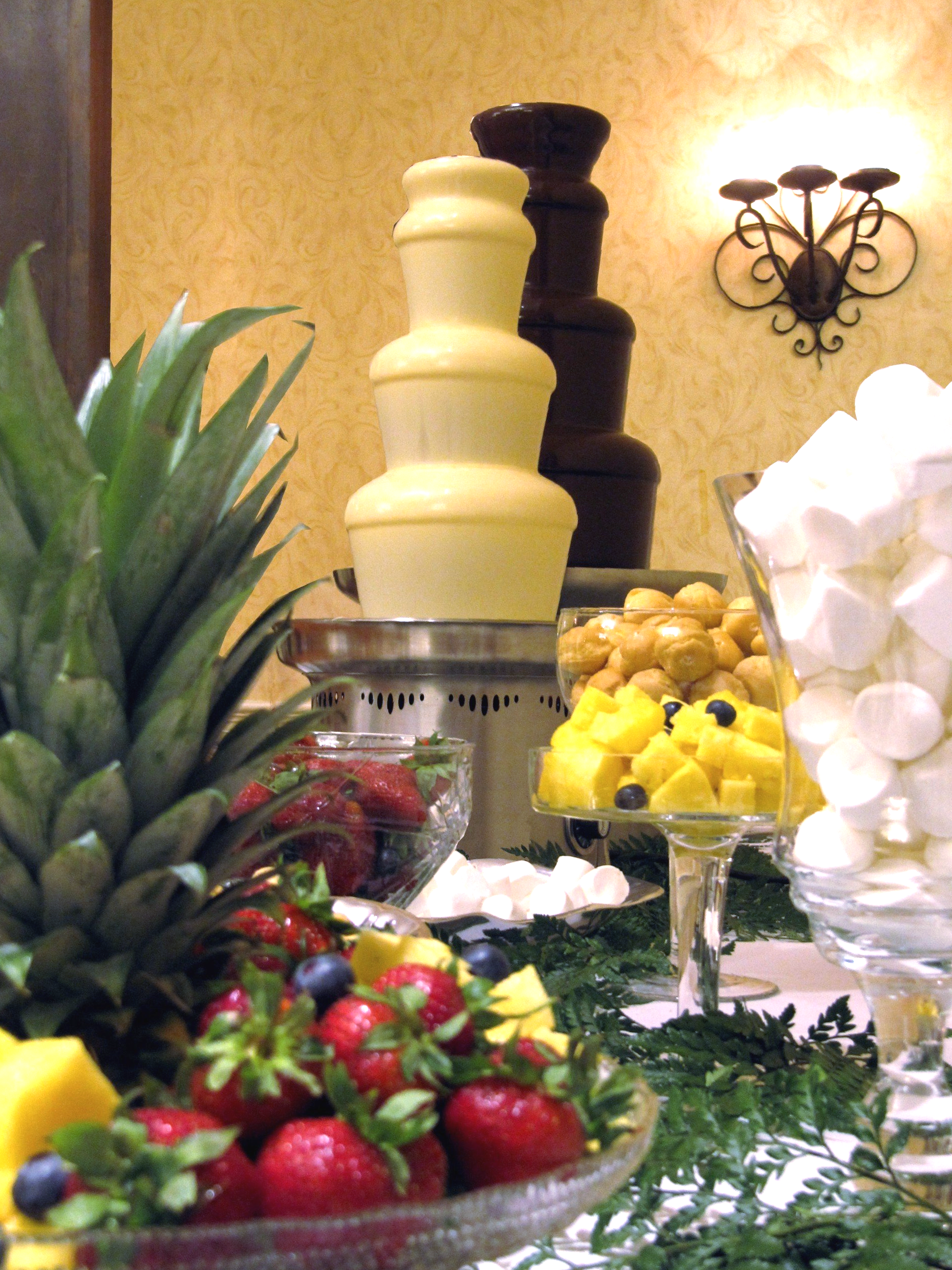 A chocolate fountain surrounded by fruit and marshmallows