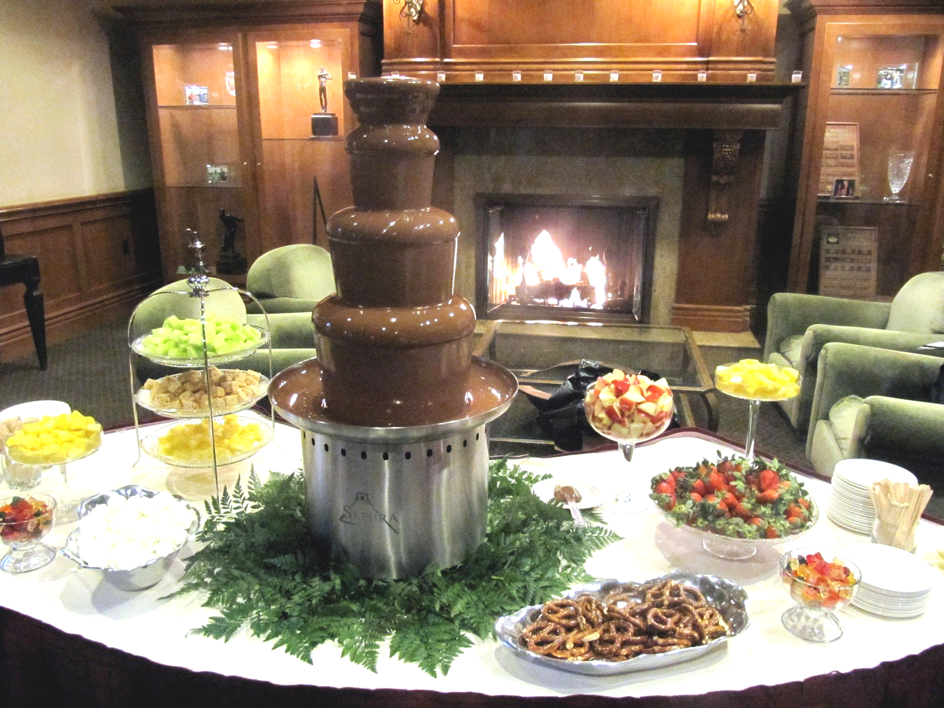 A chocolate fountain is on a table in front of a fireplace