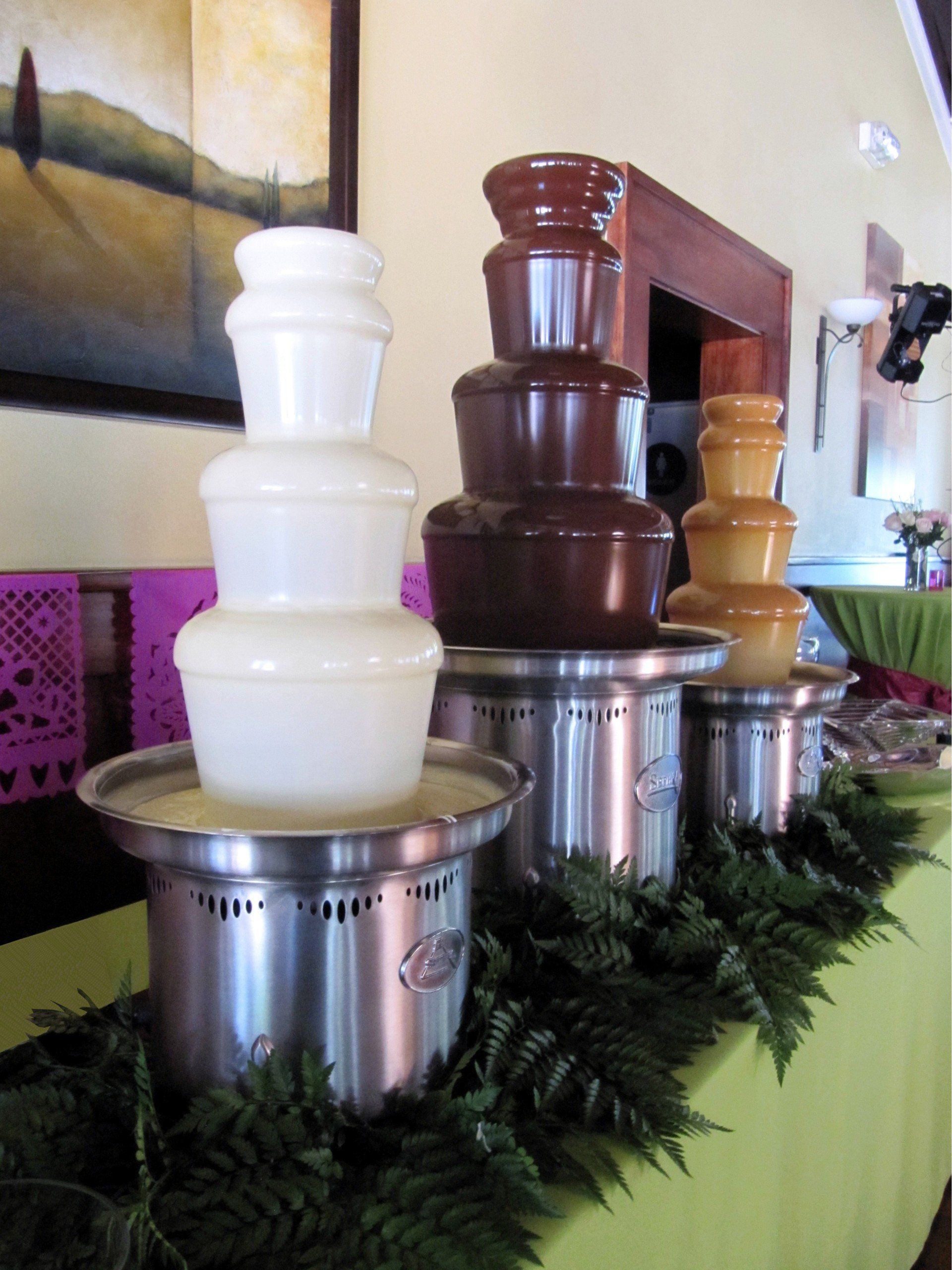 Several chocolate fountains are lined up on a table