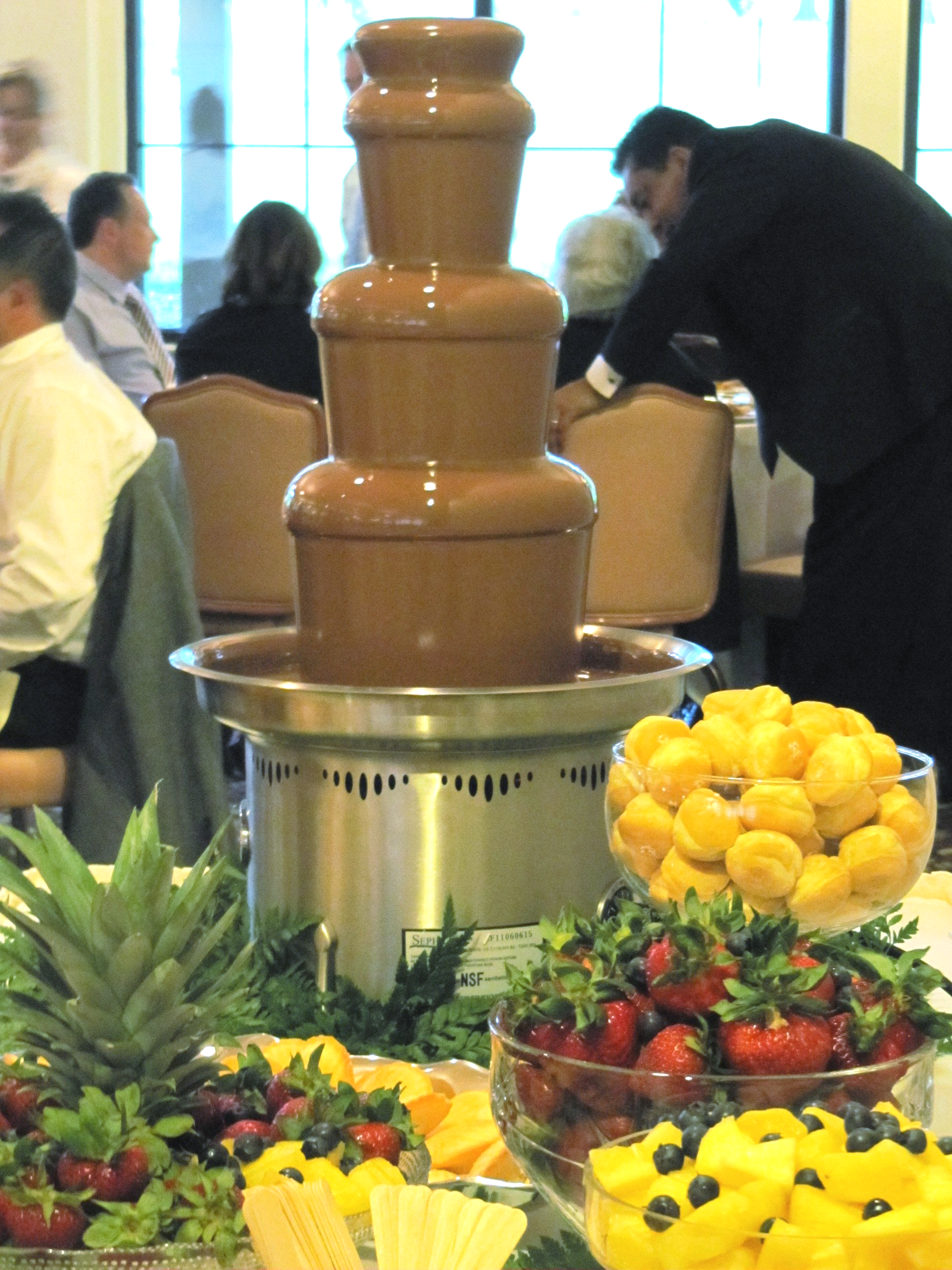 A chocolate fountain with strawberries and pineapples in front of it